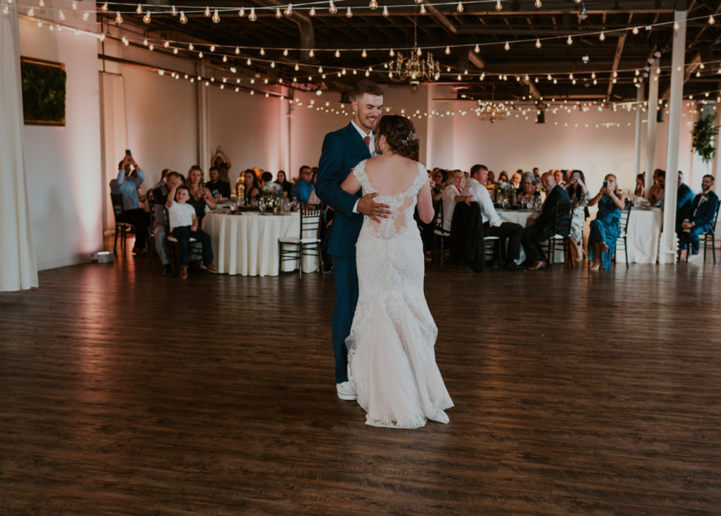 A couple is dancing at the Arbor Loft wedding venue in Rochester, facing each other with their guests sitting at tables in the background.