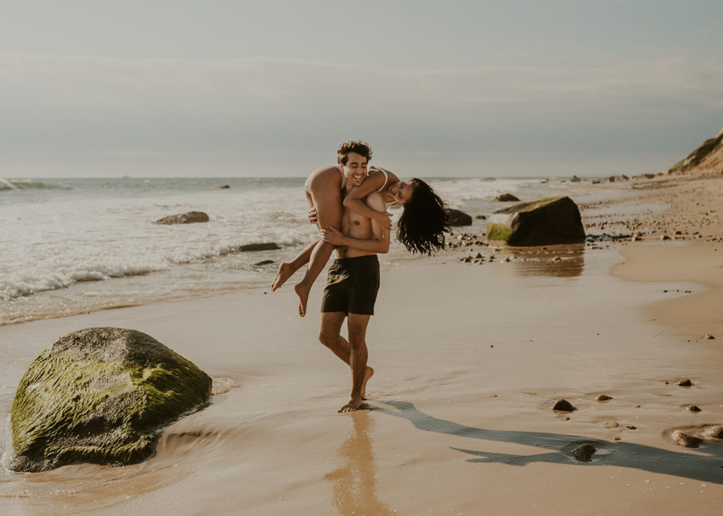 A couple is showing great examples of what to wear for engagement photos on the beach - bathing suits!