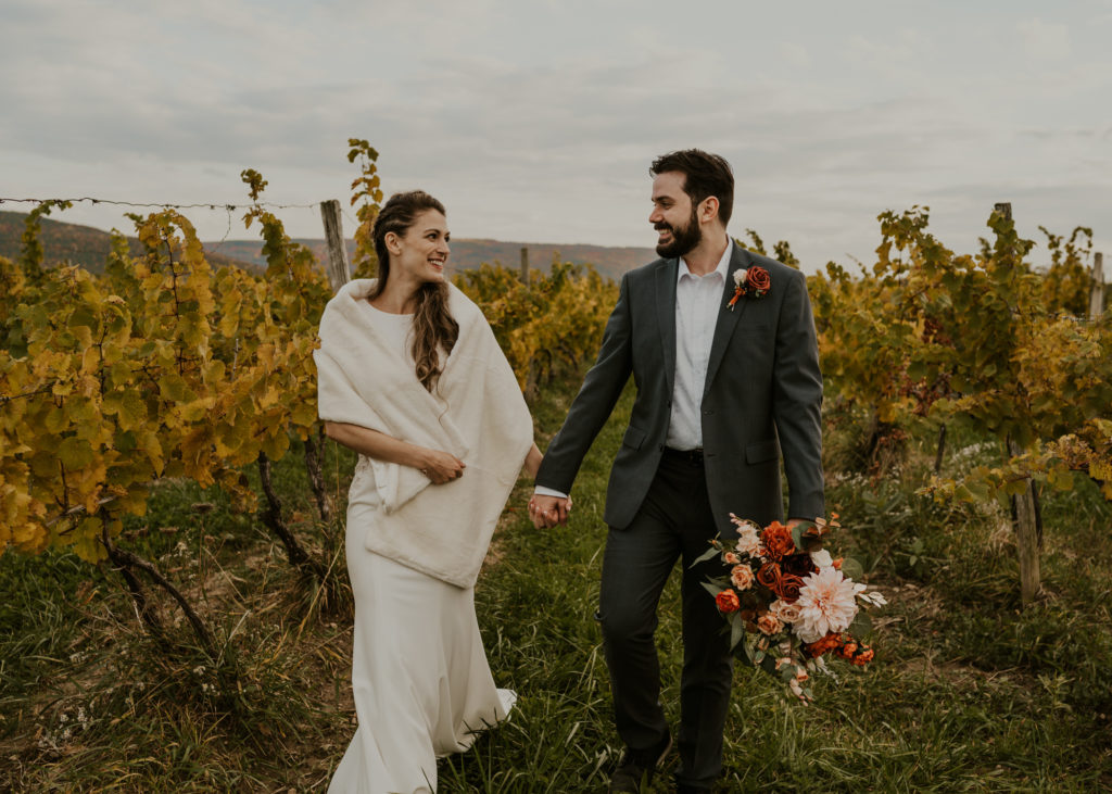 A couple walking hand in hand in front of a vineyard at their wedding venue.